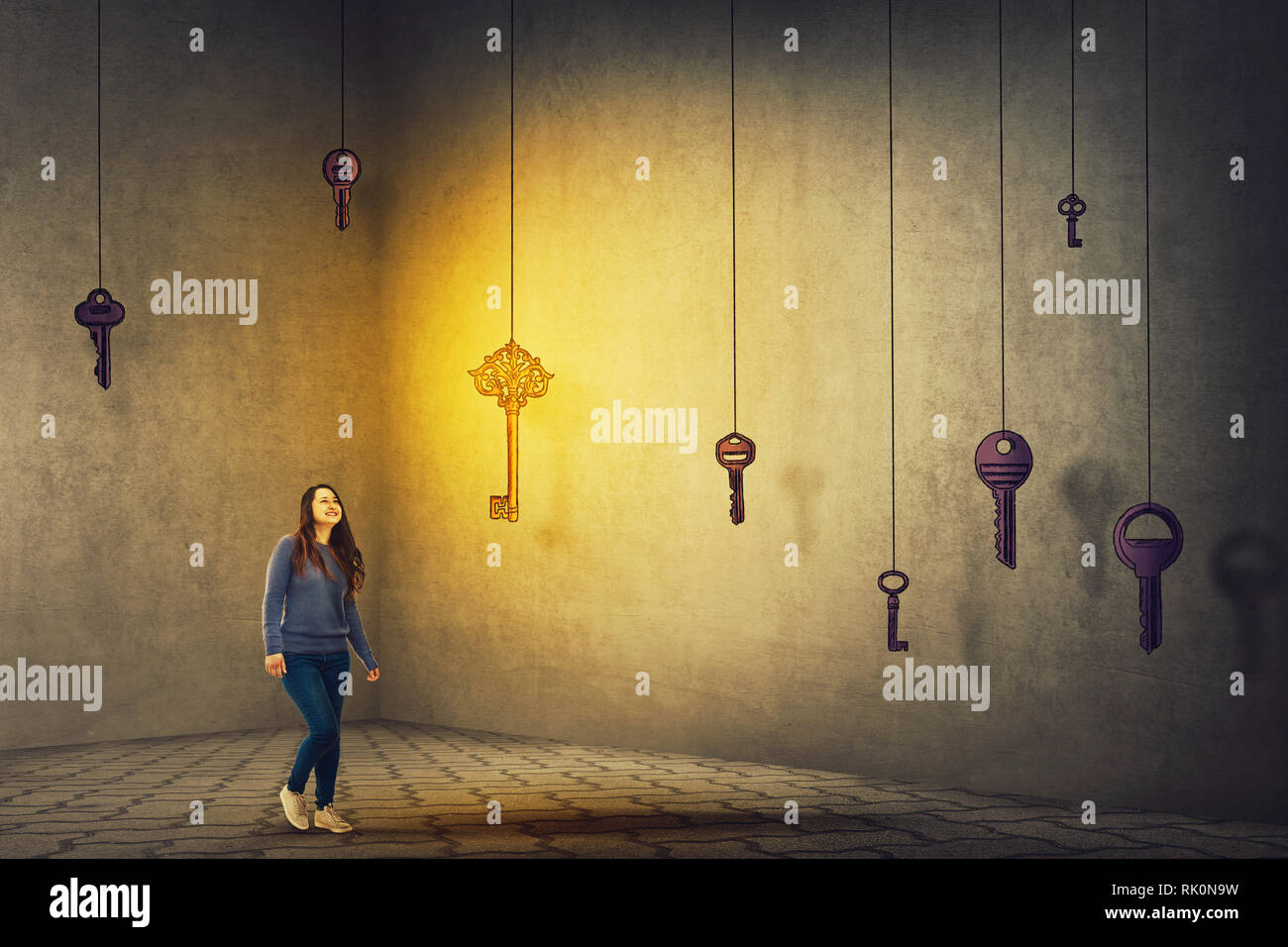 Confident young woman walking in a dark room to find the magic key to success. Concept of business aspirations, achievement and the right choice. Ambi Stock Photo