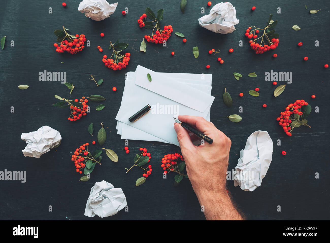 Hand writing on white blank envelope mock up copy space over dark desktop background decorated with wild berry fruit arrangement Stock Photo
