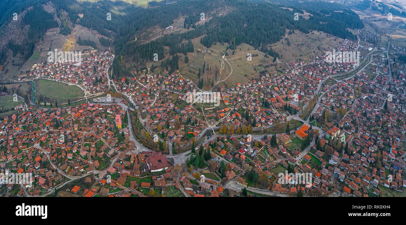 Panoramic drone view of small village in the mountains with old typical traditional houses against green hills and dynamic blue sky . Stock Photo