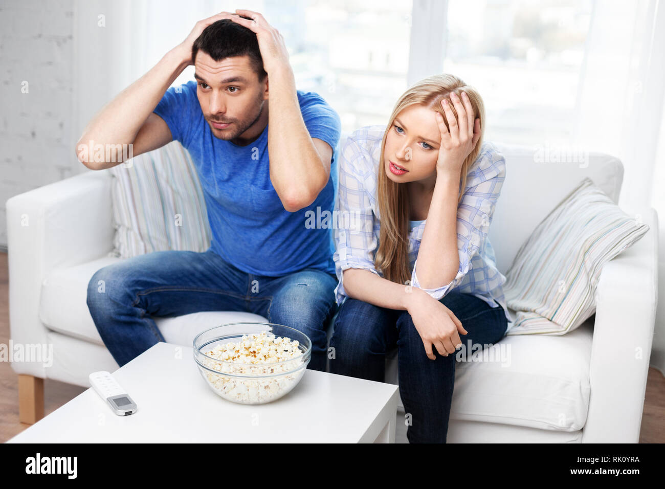 upset couple with popcorn watching tv at home Stock Photo