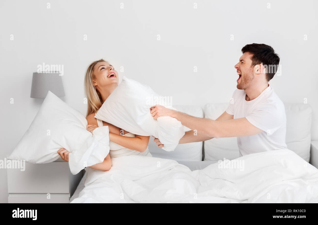 happy couple having pillow fight in bed at home Stock Photo