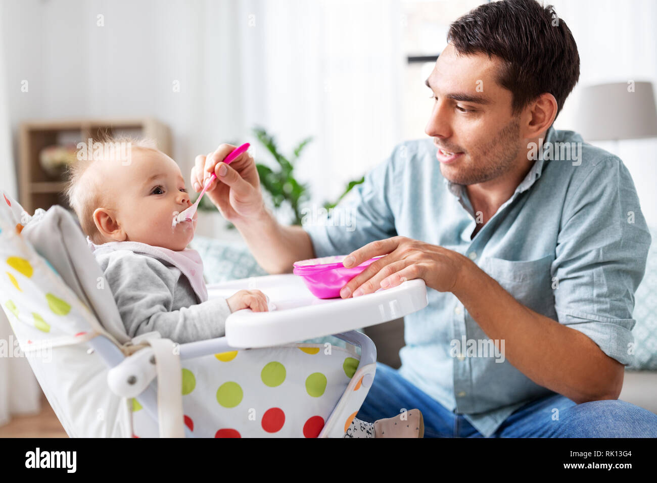 father feeding happy baby in highchair at home Stock Photo