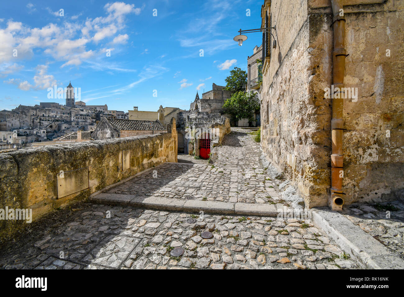 Typical forked hillside path with a red door near the Convent of Saint Agostino in the ancient city of Matera, Italy, with the church tower visible in Stock Photo