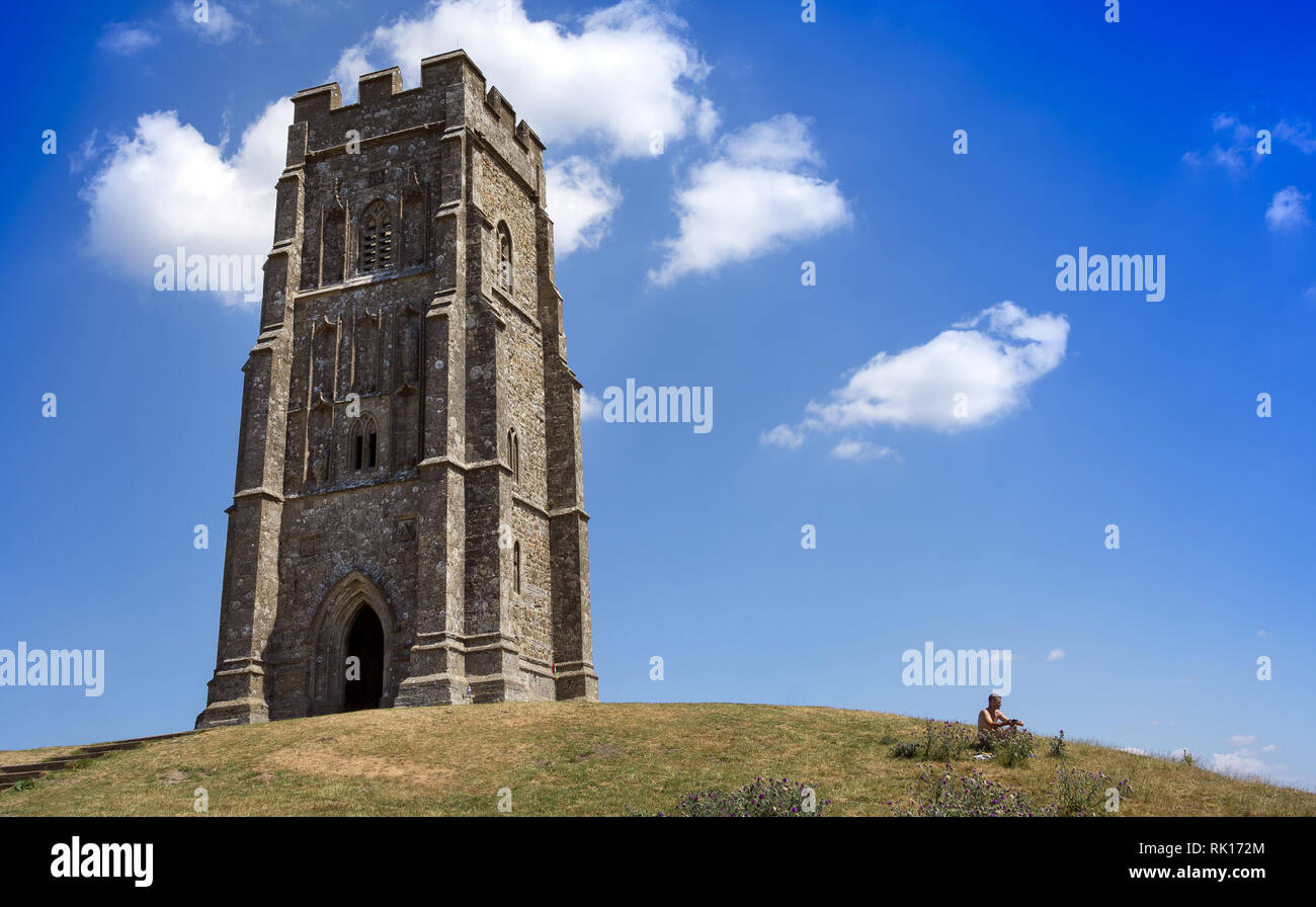 Man soaking up the sun on top of Glastonbury Tor next to St Michael's Tower, Somset, England, UK Stock Photo