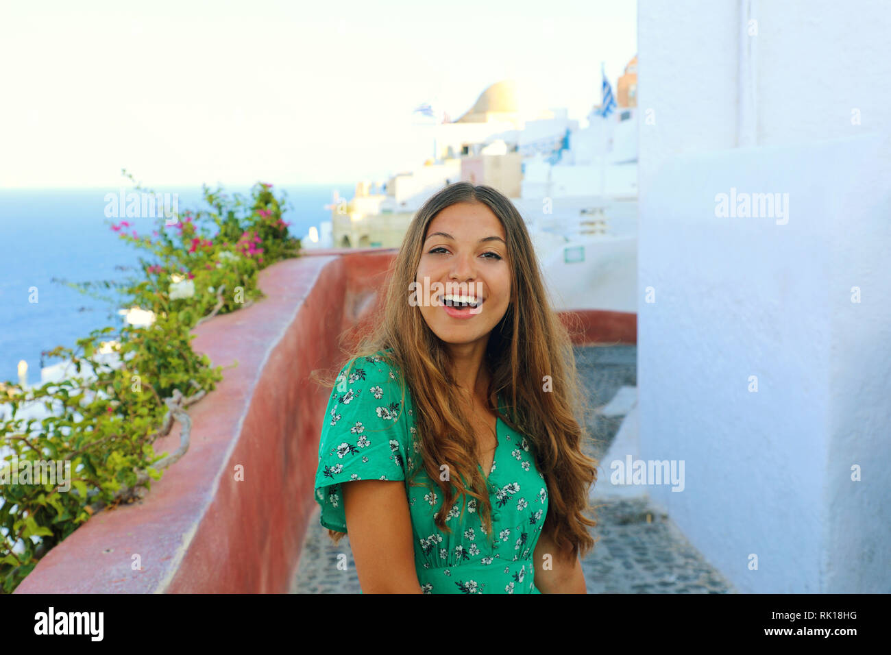 Santorini cheerful travel tourist woman visiting famous white village of Oia. Smiling tanned girl in green dress in Santorini, Cyclades, Greece. Stock Photo