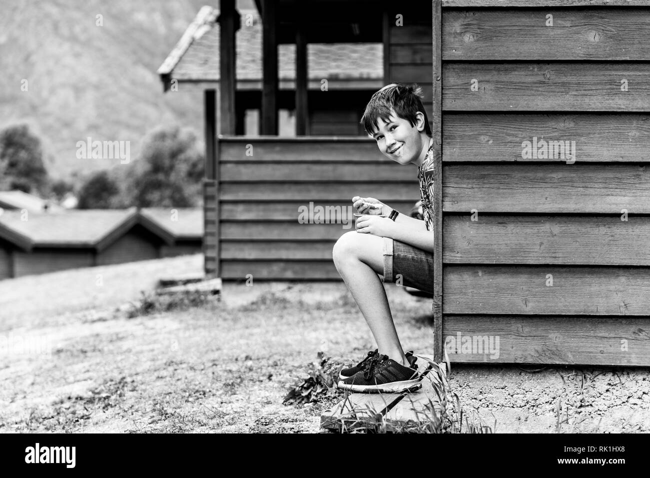 Portrait of boy sitting on steps by holiday chalet, black and white image, Flam, Norway, Europe Stock Photo