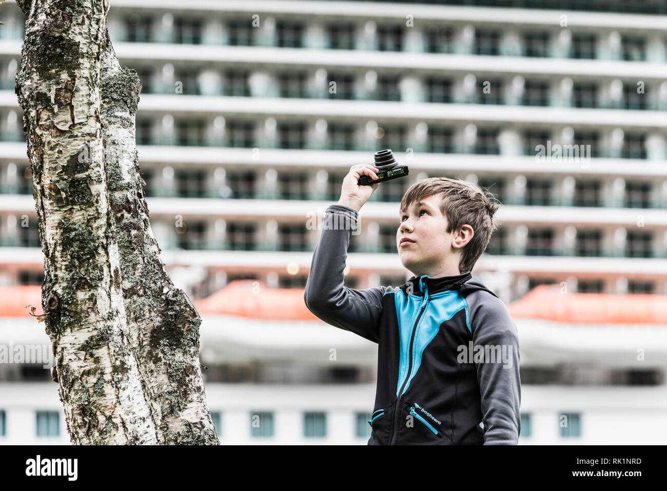 Portrait of young boy pointing camera upwards by tree Stock Photo
