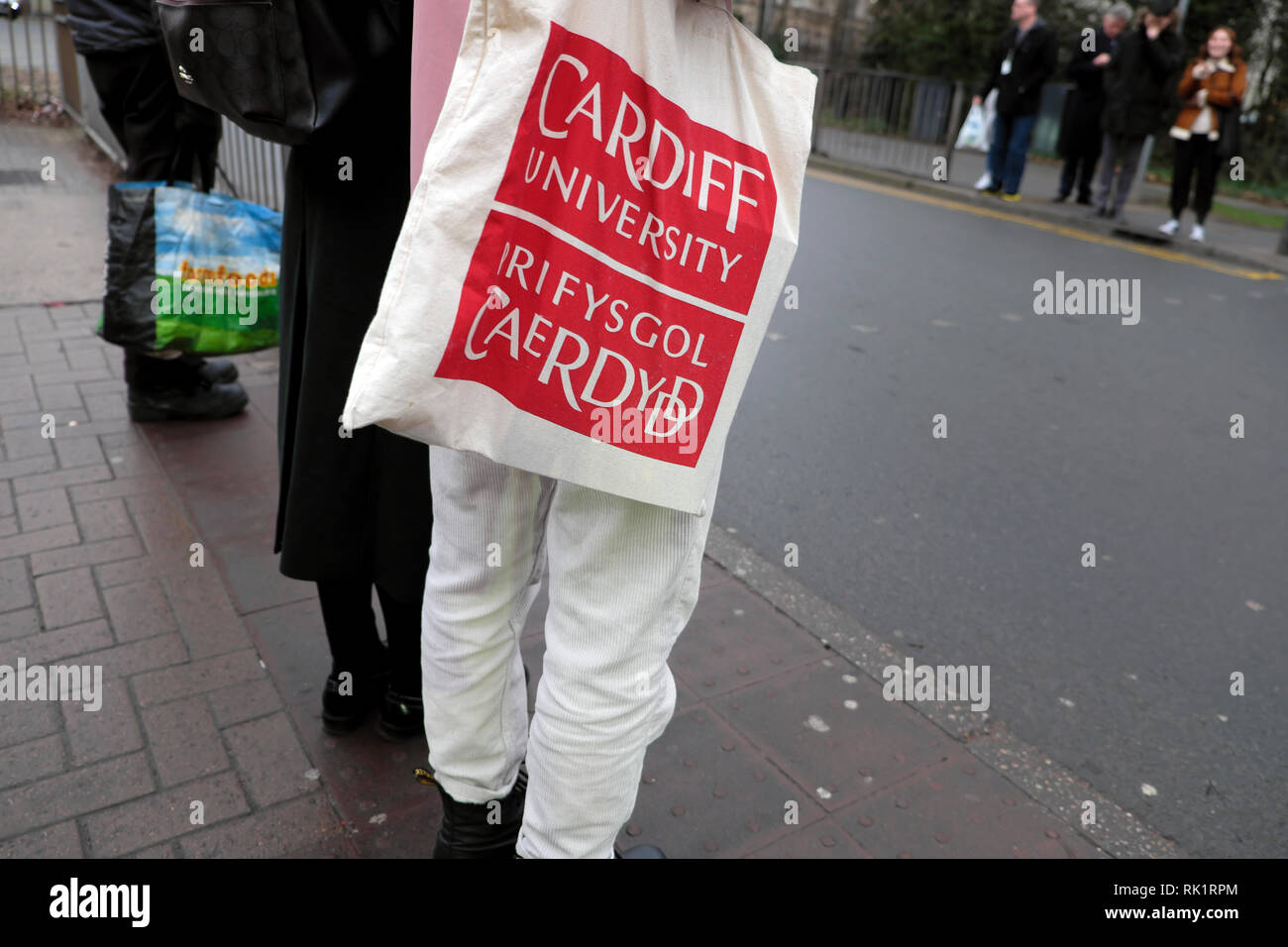 A person with a Cardiff University bilingual English Welsh language canvas shoulder bag waiting to cross the road in Cardiff Wales UK  KATHY DEWITT Stock Photo