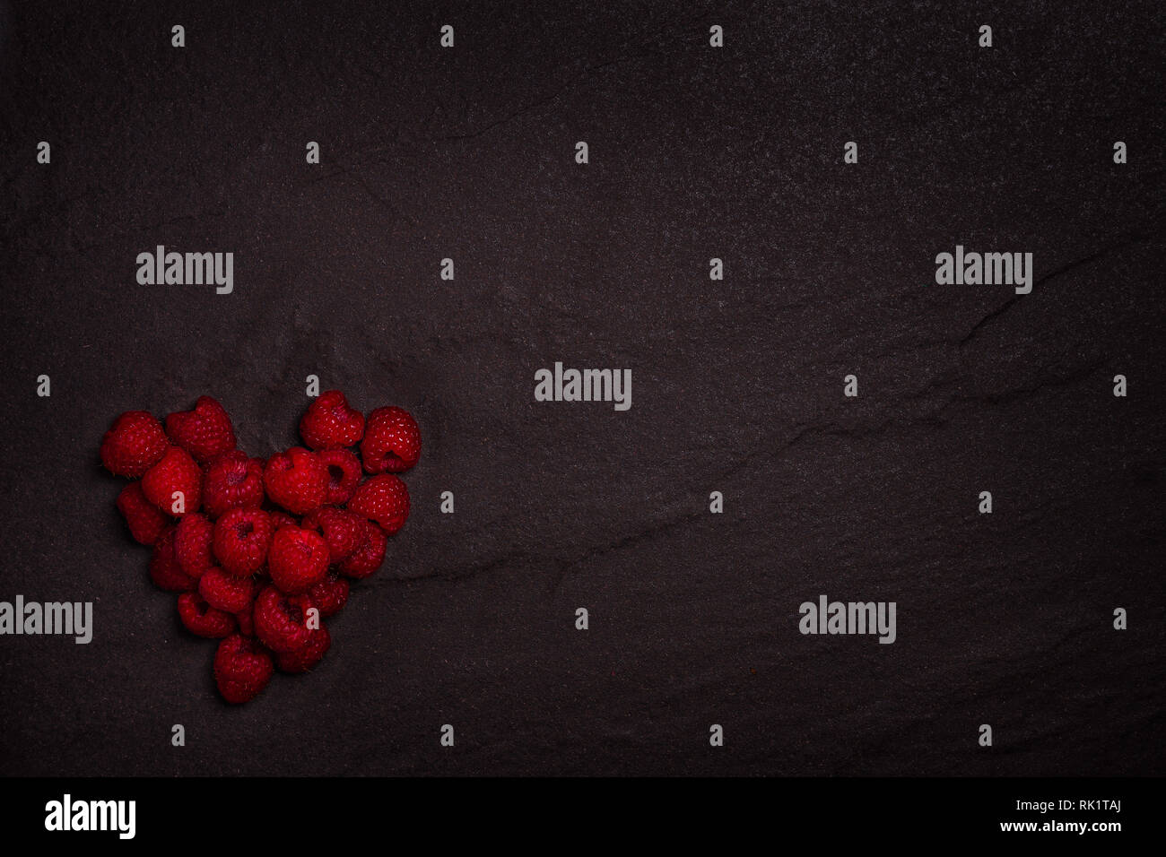 Fresh organic raspberries in a heart shape on a dark rock background ...