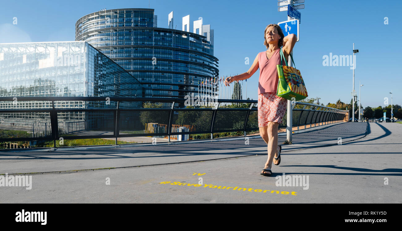 STRASBOURG, FRANCE - SEP 12, 2018: Woman walking in front of large protest banner Save Your Internet with European Parliament in the background early in the morning Stock Photo
