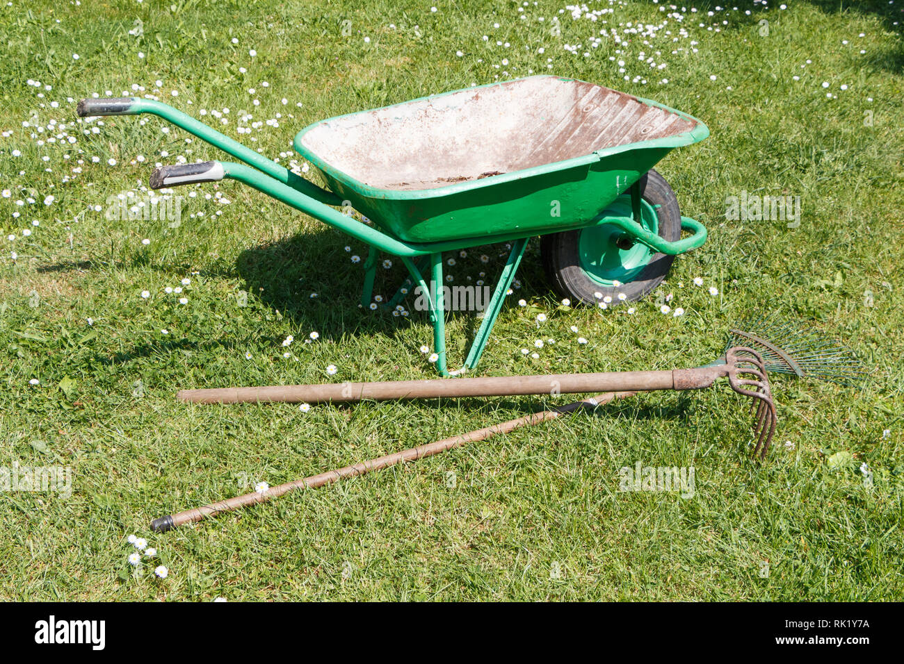 Green wheelbarrow with lawn rake and claw cultivator in a garden Stock Photo