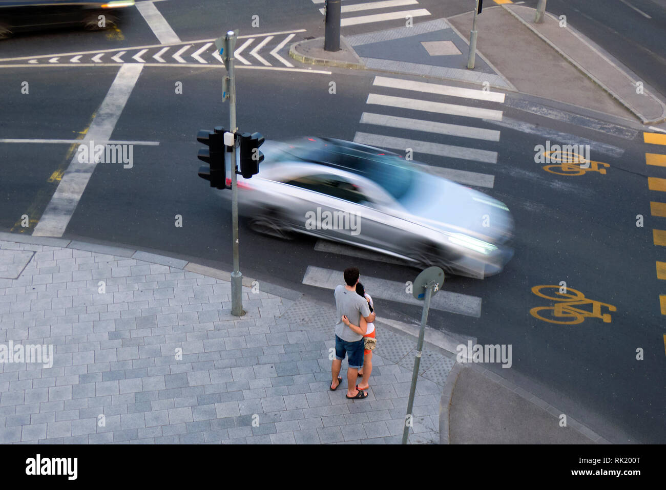 Young couple standing hugging in front of crossroad with blurred moving car. Top view Stock Photo