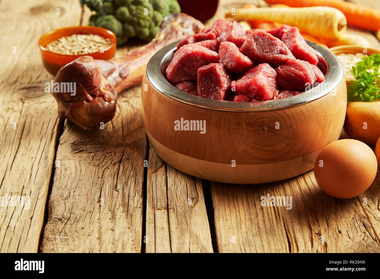 Pet food in a wooden bowl with fresh meat, bone, egg and vegetables for a healthy diet for carnivores such as cats and dogs Stock Photo