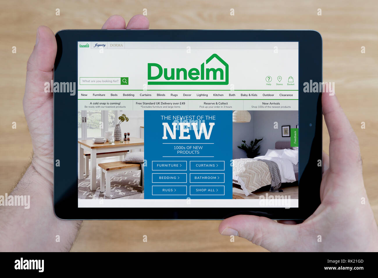 A man looks at the Dunelm website on his iPad tablet device, shot against a wooden table top background (Editorial use only). Stock Photo