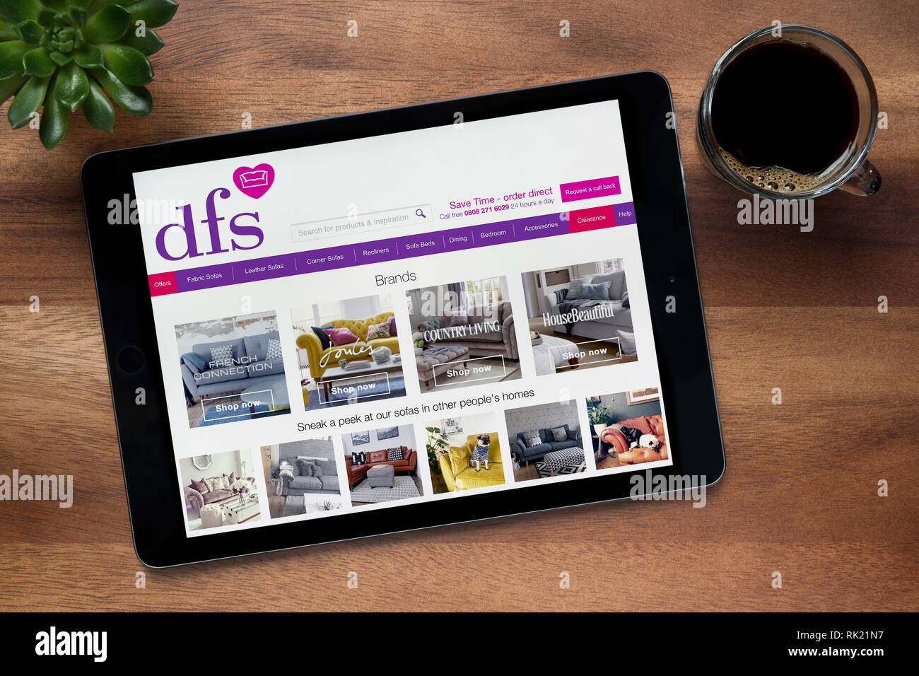 The website of dfs is seen on an iPad tablet, on a wooden table along with an espresso coffee and a house plant (Editorial use only). Stock Photo