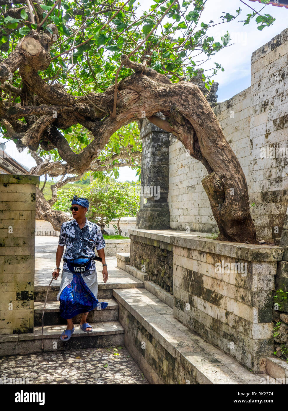 An Indonesian man wearing a sarong walking in a courtyard in Uluwatu temple compound, Bali Indonesia. Stock Photo