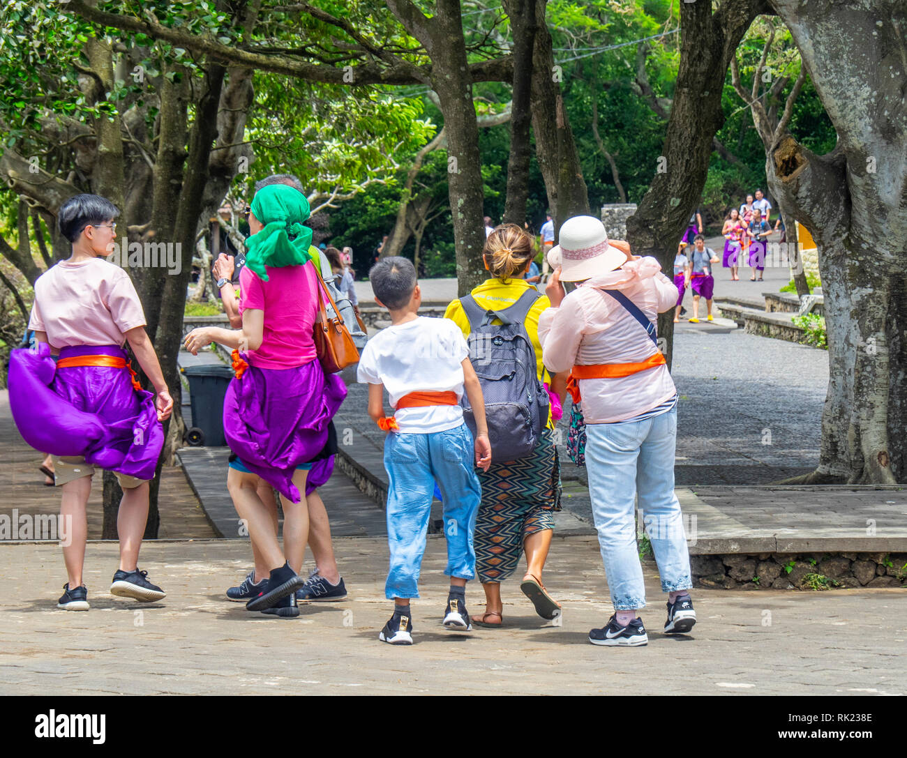 Chinese tourists wearing purple sarongs visiting Uluwatu Temple  Bali Indonesia. Stock Photo
