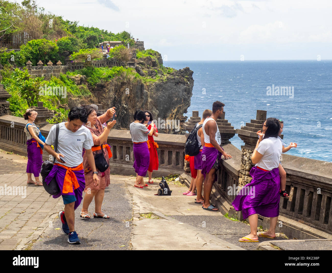 Chinese tourists wearing purple sarongs visiting Uluwatu Temple  Bali Indonesia. Stock Photo