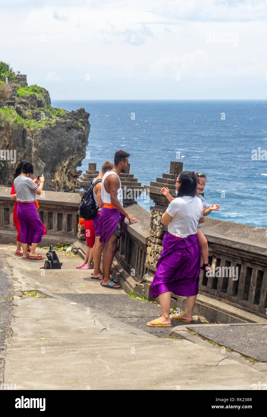 Chinese tourists wearing purple sarongs visiting Uluwatu Temple  Bali Indonesia. Stock Photo