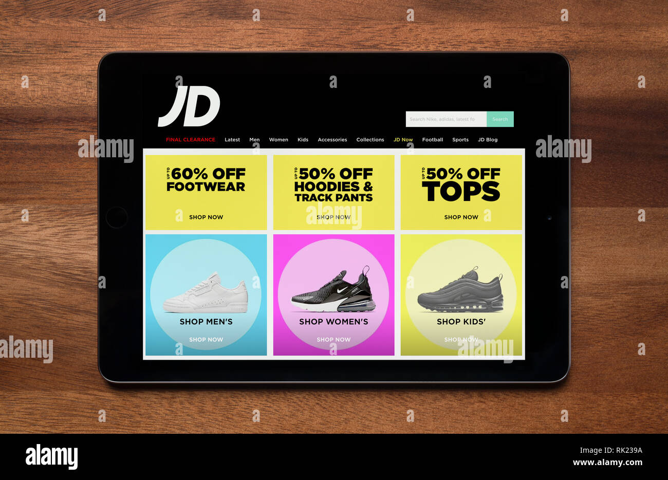 The website of JD Sports is seen on an iPad tablet, which is resting on a wooden table (Editorial use only). Stock Photo