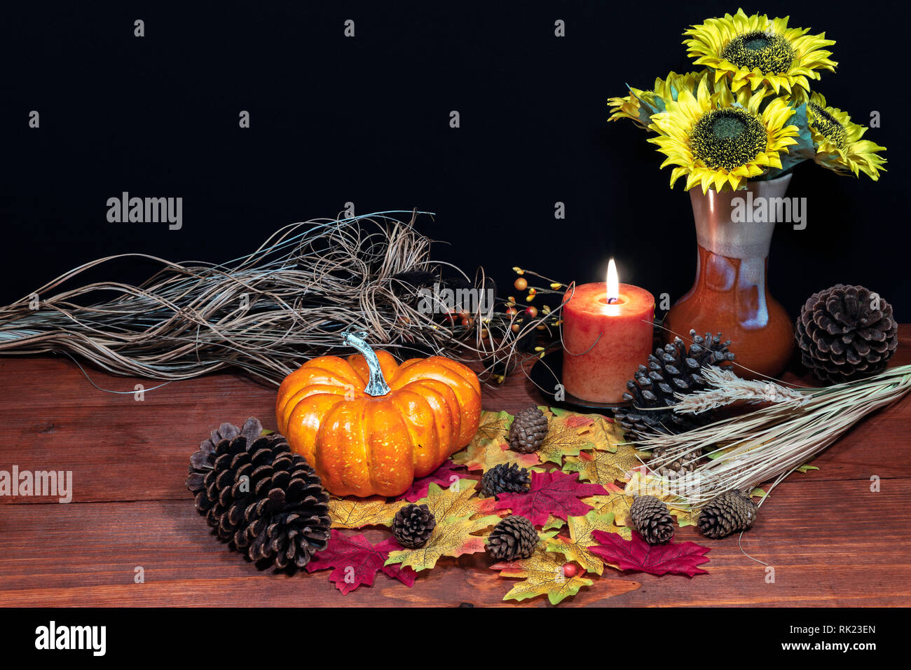 Silk maple leaves, beautiful bouquet of sunflowers, frosted pinecones and orange candle on tabletop with dark background. Stock Photo