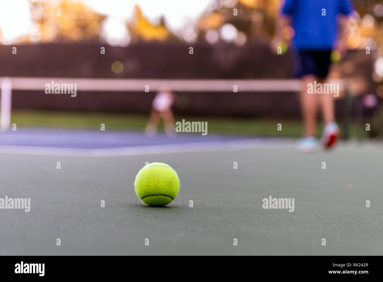 Lone yellow tennis ball lying out of bounds during a private racket club tennis lesson. Stock Photo