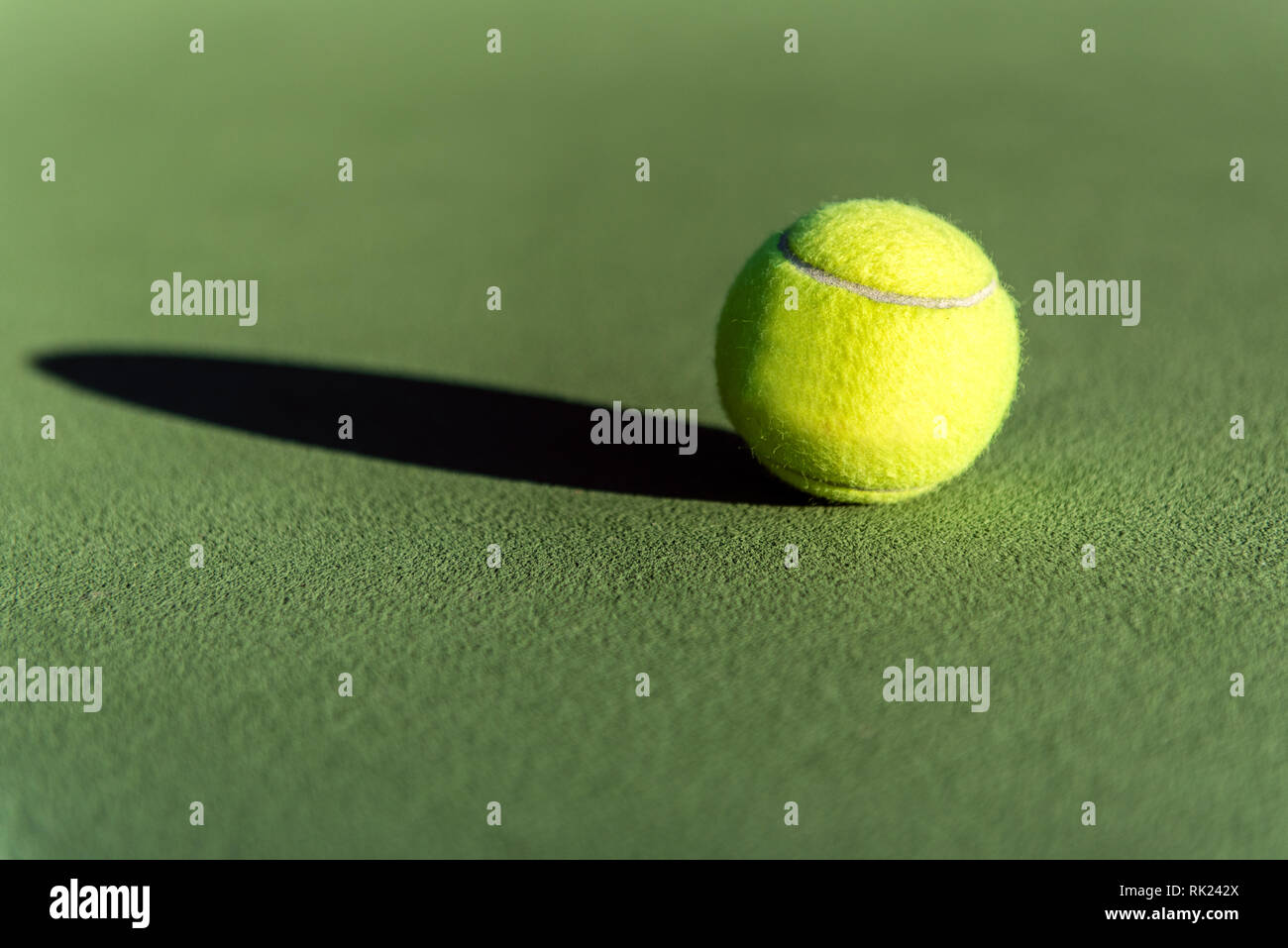 Fuzzy yellow tennis ball lying on the textured surface of court over a long shadow. Stock Photo