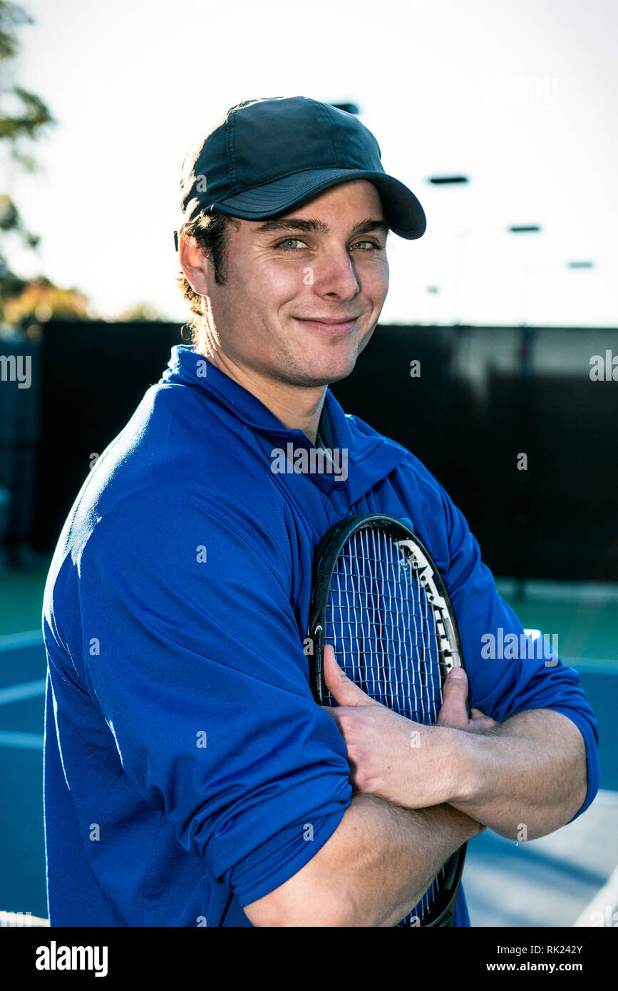 Confident young and good looking tennis teaching professional showing a smirky smile and on the tennis court. Stock Photo