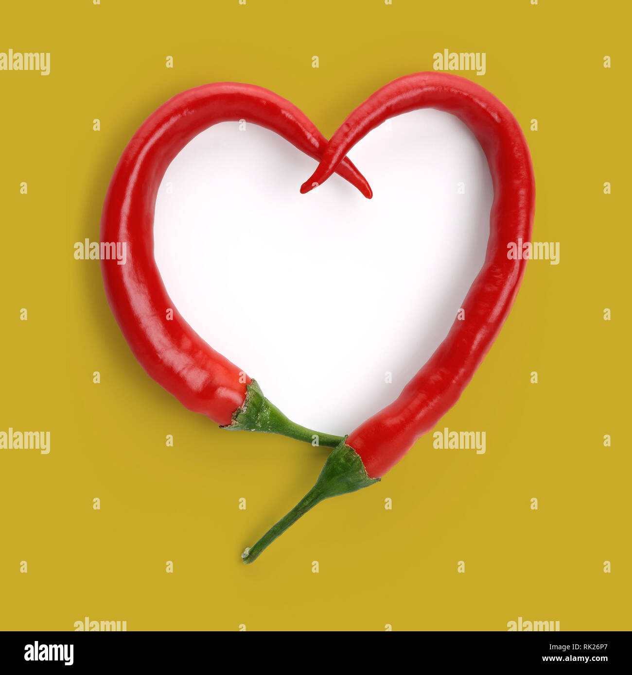 Heart shape made of red peppers, isolated on mustard colour background