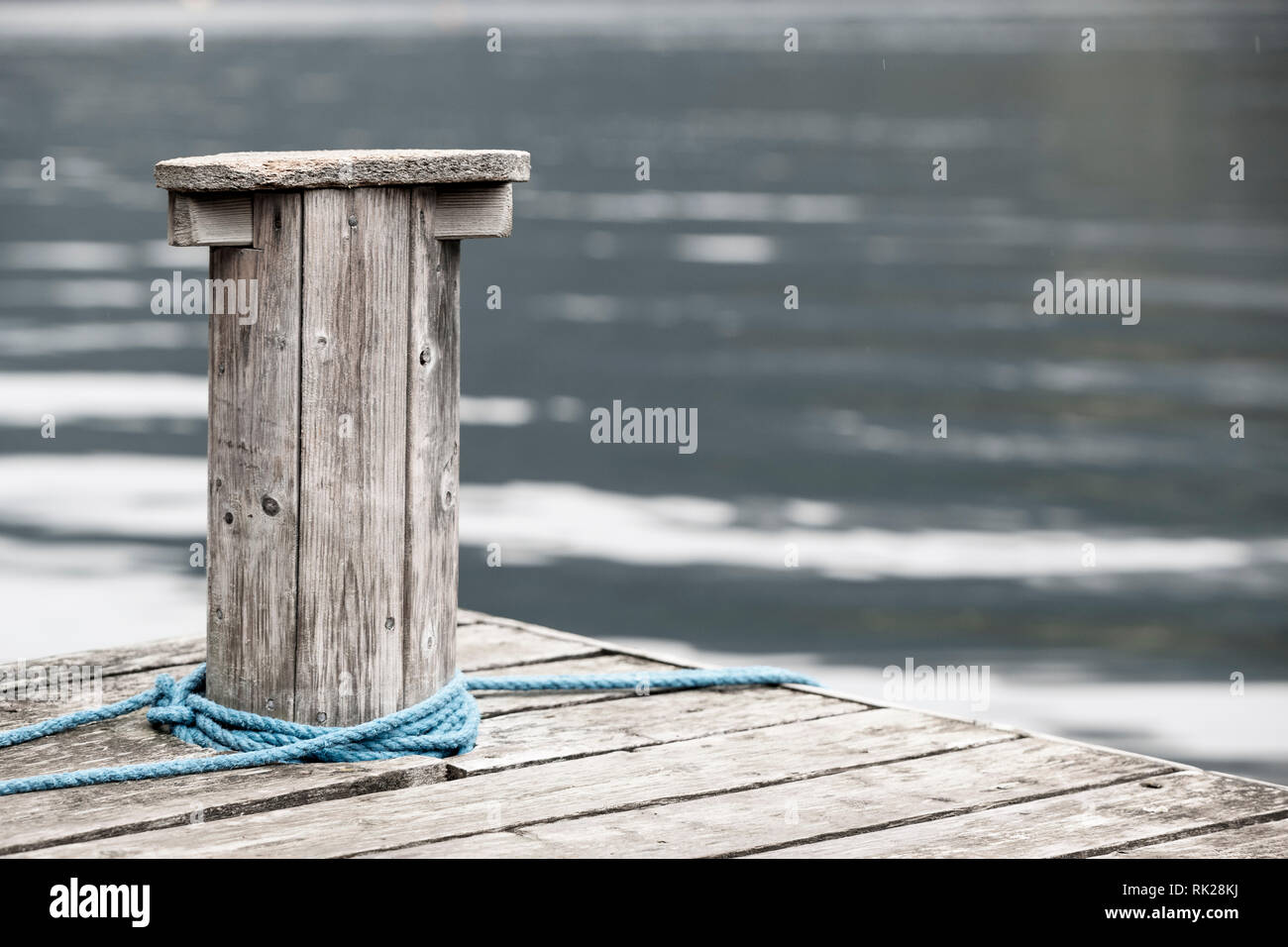 Blue rope wrapped around wooden post by rippling water Stock Photo