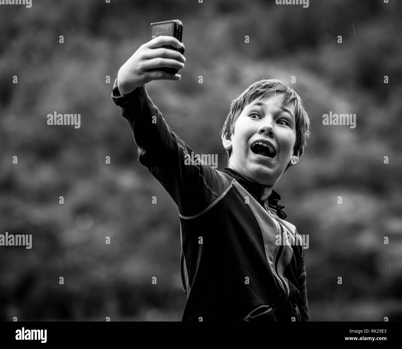Candid portrait of young boy taking selfie outdoors using smart phone, black and white image Stock Photo