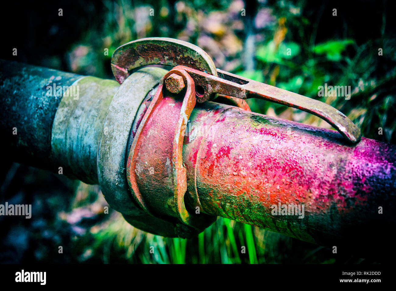 Old colorful metal pipes with clutch on dark background with blurred grass. Coupling of red and blue pipeline close-up. Cohesiveness, fixed connection. Stock Photo