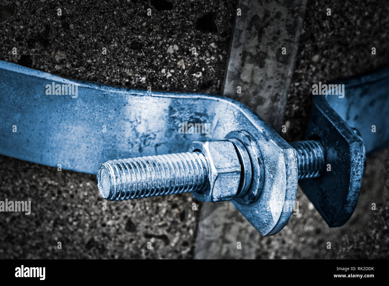 Close-up of a metal bolt shaft with spiral screw thread and hexagon nut on a concrete pole. Steel bolted joint with blue hoop on dark gray background. Stock Photo