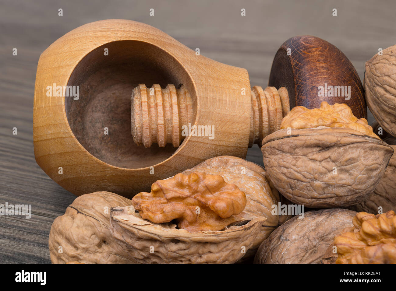 Cracking of walnuts with a wooden screw nutcracker in mushroom shape. Close-up of the kitchen tool and a group of partly peeled nuts with half shells. Stock Photo