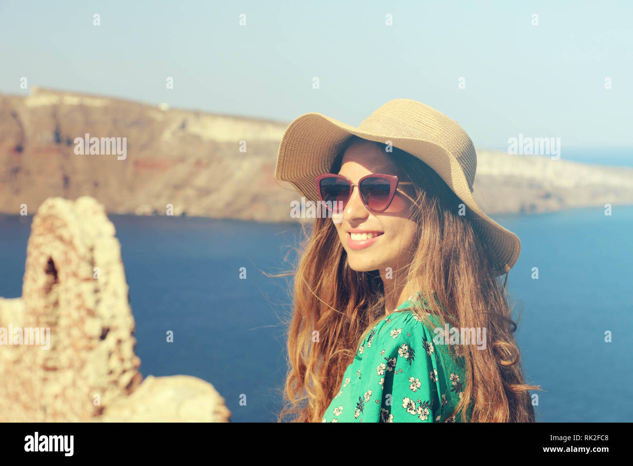 Beautiful young woman with hat and sunglasses enjoying the sun in Santorini with the Caldera on background, Greece, Europe. Vintage filter. Stock Photo