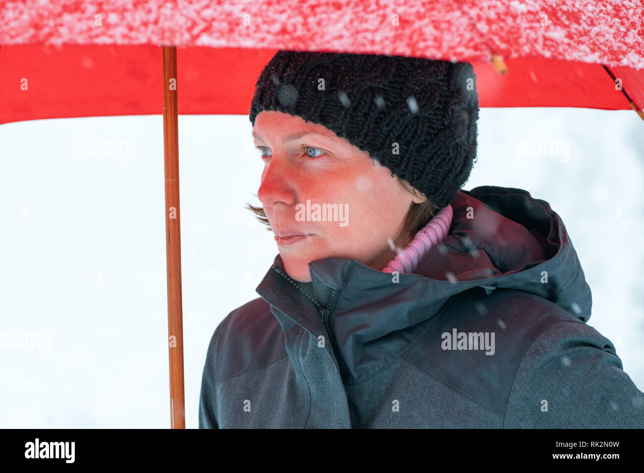 Sad disappointed woman in standing in winter snow under big red umbrella Stock Photo