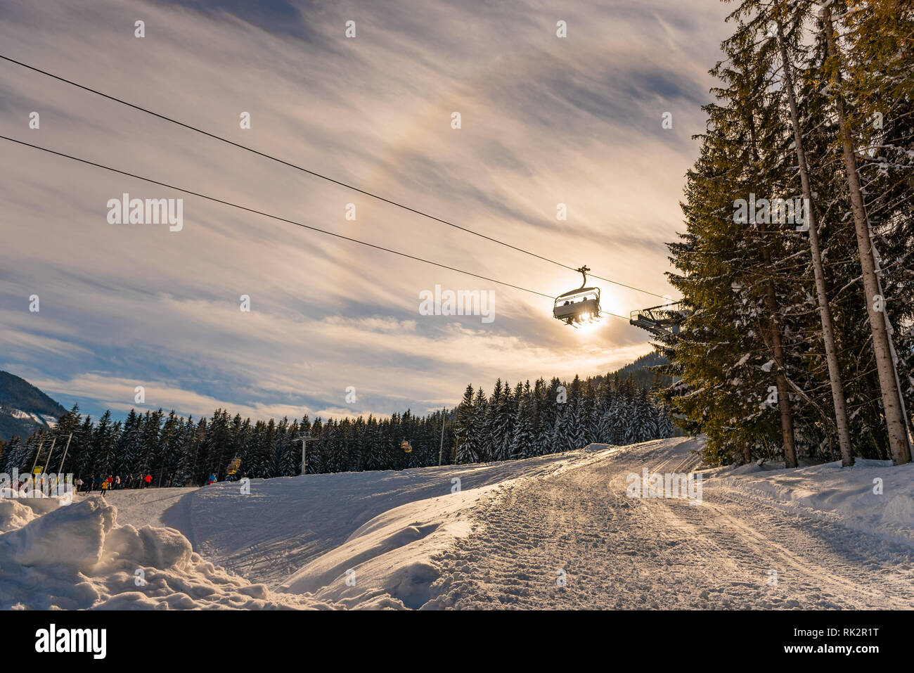 Four skiers on a chair lift against the backdrop of the sun and trees, contour photo, orange shades and halo atmospheric optical phenomenon effect. Stock Photo