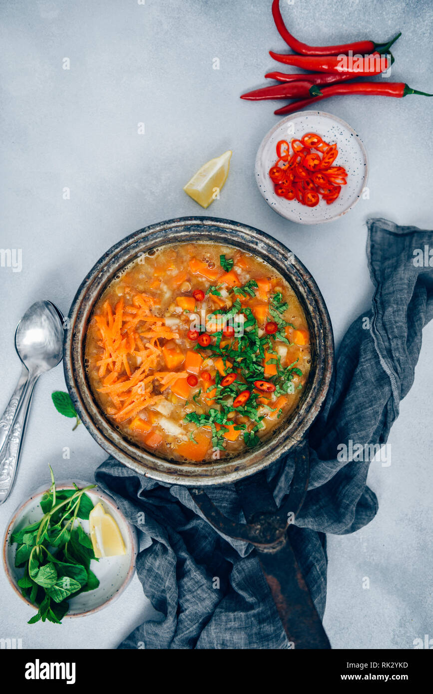 Carrot soup with lentils and rice in a vintage pan garnished with chopped fresh mint and chili peppers photographed on a light grey background from to Stock Photo