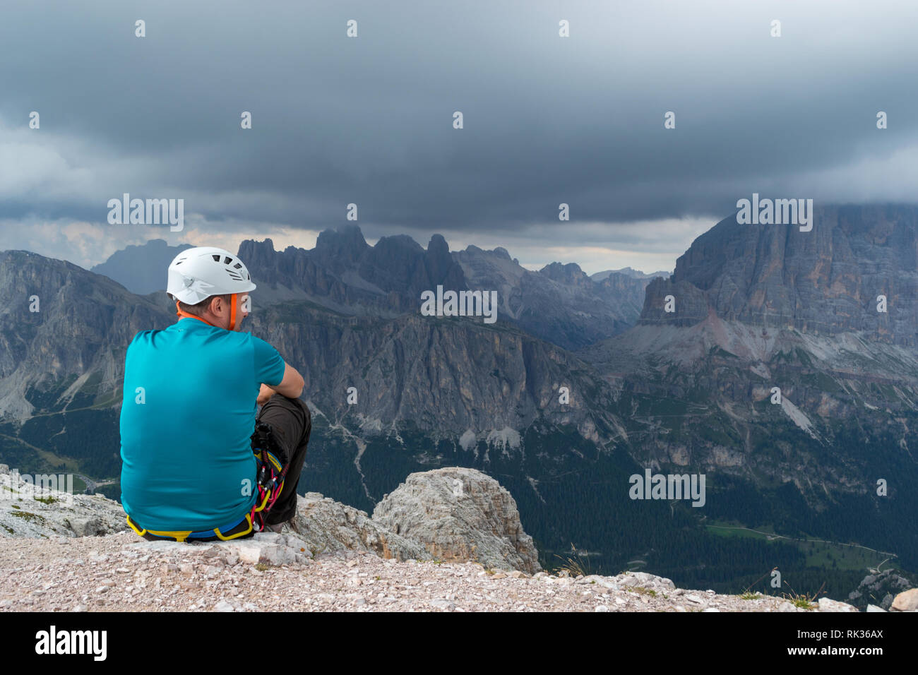 A man pausing after a via ferrata climb on top of Averau mountain peak, in Dolomites, Italy, gazing at the incoming storm clouds Stock Photo