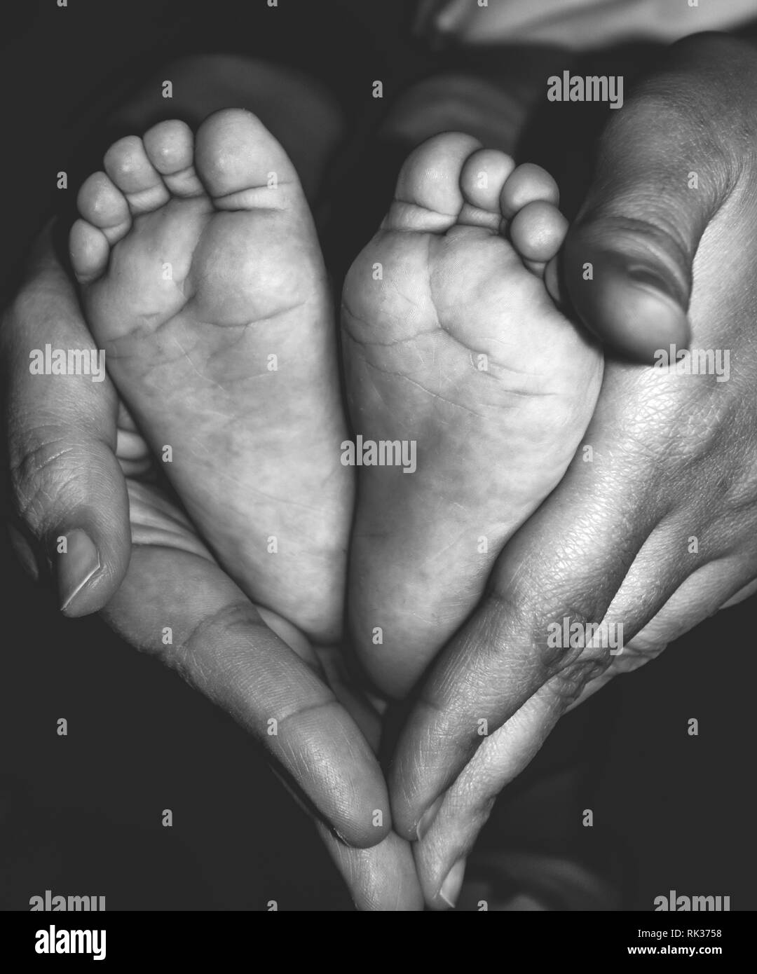 Baby feet in mother hands. Tiny Newborn Baby's feet on female Heart Shaped hands closeup. Beautiful Black and White conceptual image of Maternity. Stock Photo