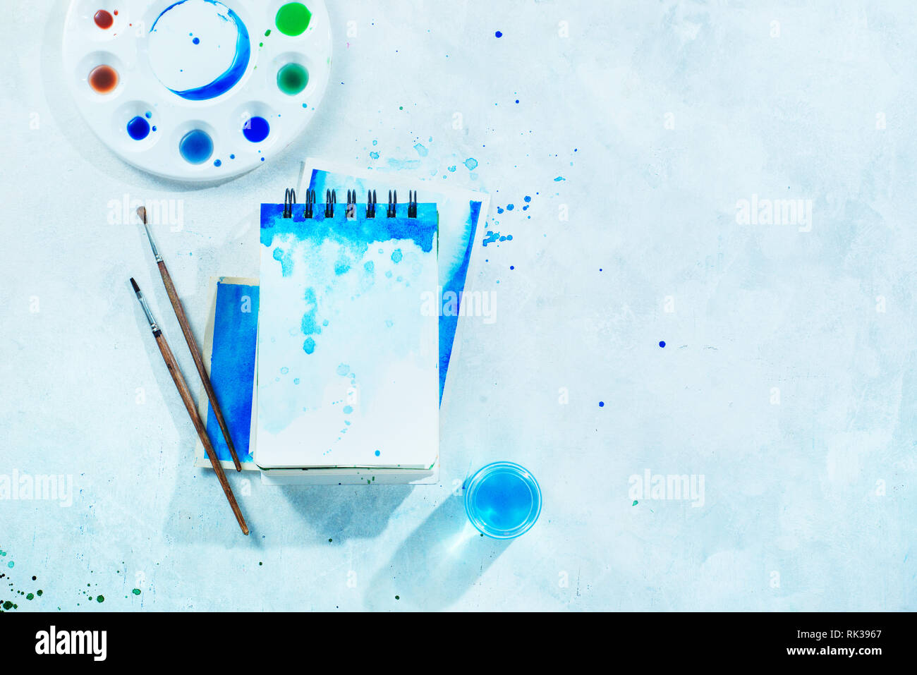 Painting spring concept with artist tools, green and blue watercolor sketchbooks, brushes and color palette on a white background with copy space Stock Photo