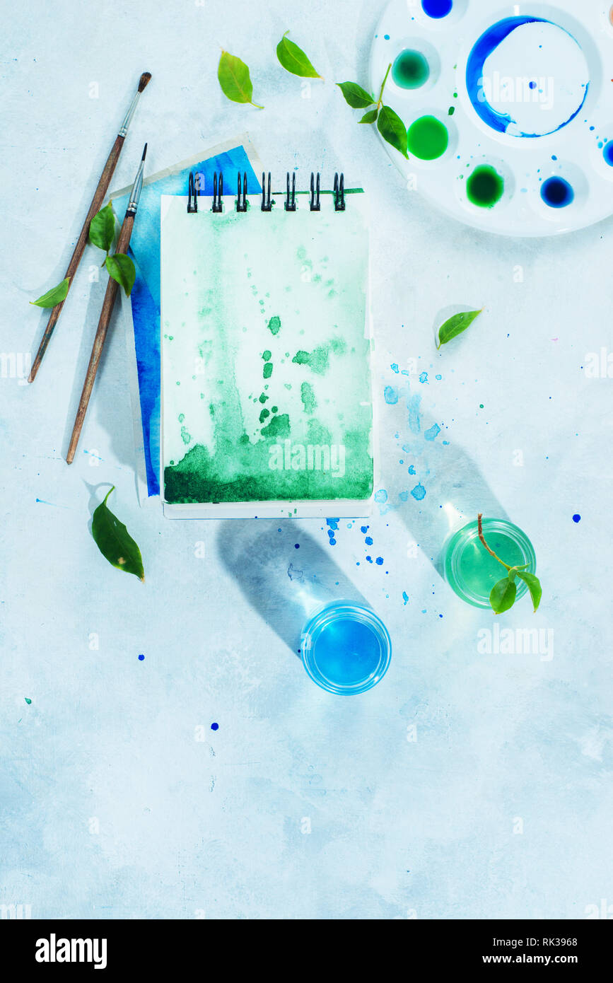 https://c8.alamy.com/comp/RK3968/drawing-spring-concept-with-artist-tools-green-and-blue-watercolor-sketchbooks-brushes-and-color-palette-on-a-light-background-with-copy-space-RK3968.jpg