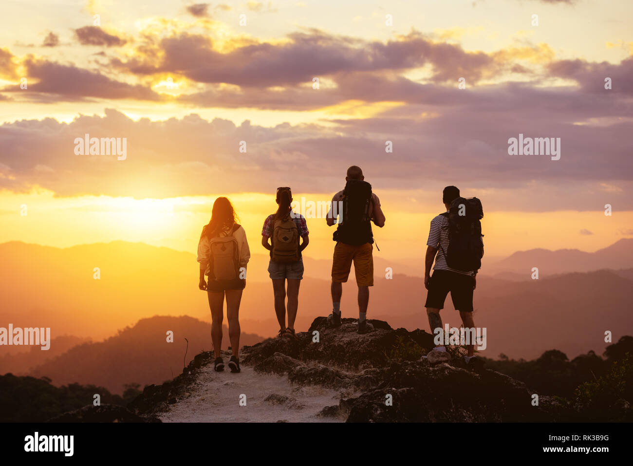 Group of four peope's silhouettes stands on mountain top and looks at sunset Stock Photo