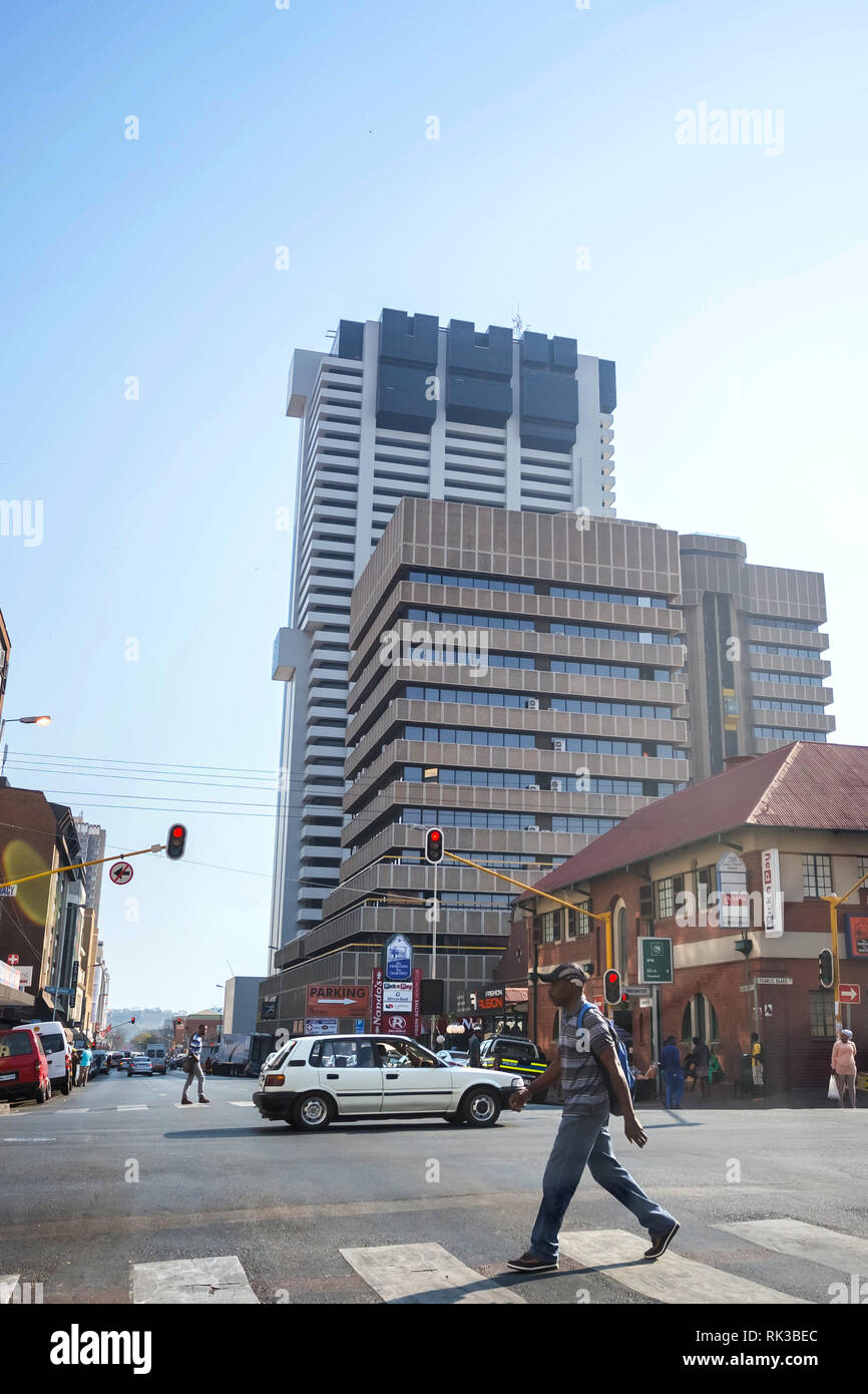 Pretoria, South Africa, 22 August - 2018: Man crossing road at traffic lights with skyscrapers in background. Stock Photo