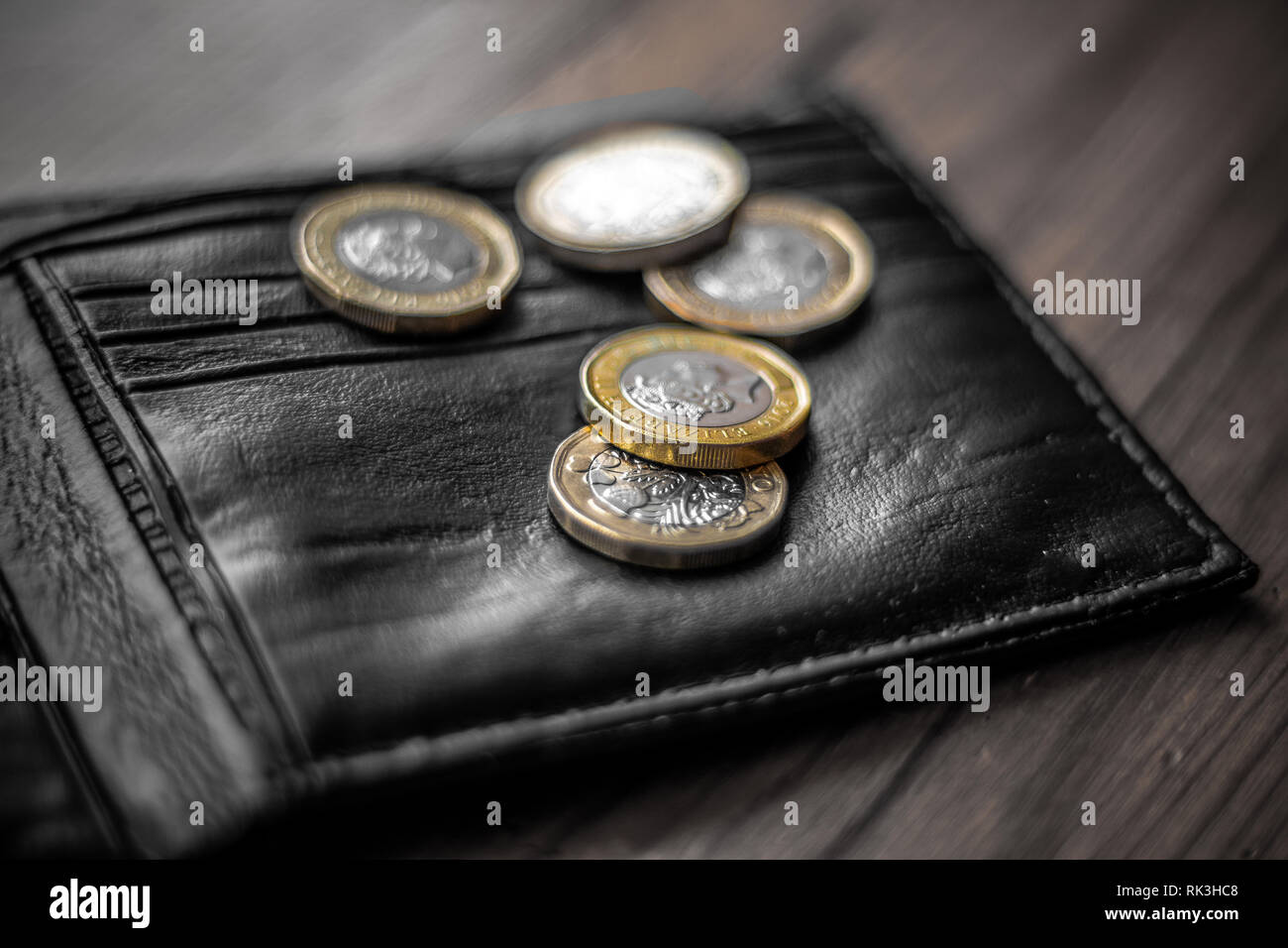 New Great British Pound GBP Coins laying casually on top of black wallet on wooden surface. Wealth, Money, Cash, Change. Stock Photo