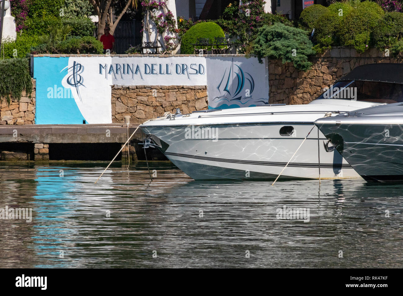 Marina dell'Orso di Poltu Quatu, in the Costa Smeralda. Close up View of Hotel and Restaurant with Moored Boat Prows and Reflections. Sardinia, Italy. Stock Photo
