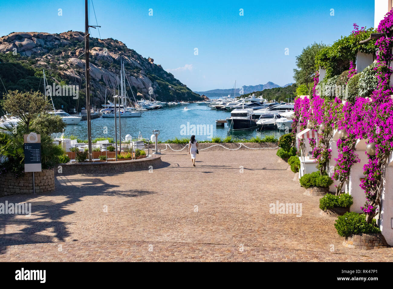 Quayside View With a Woman Looking Out from the Hotel at Moored Boats and the Landscape at Marina dell' Orso di Poltu Quatu. Stock Photo