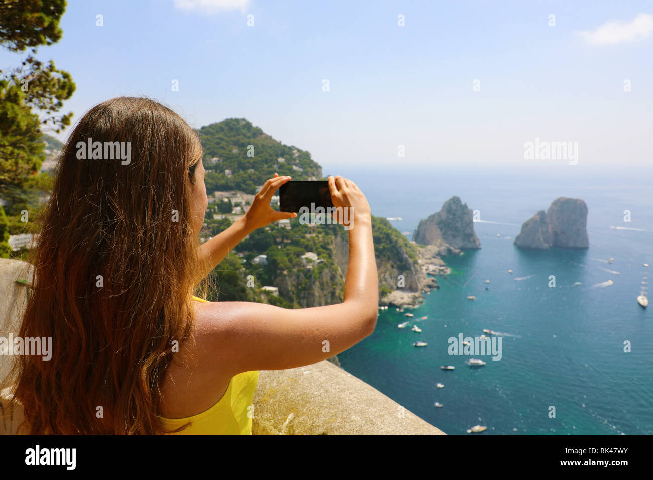 Beautiful girl taking picture in Capri Island with Faraglioni sea stack and blue crystalline water, Capri, Italy Stock Photo
