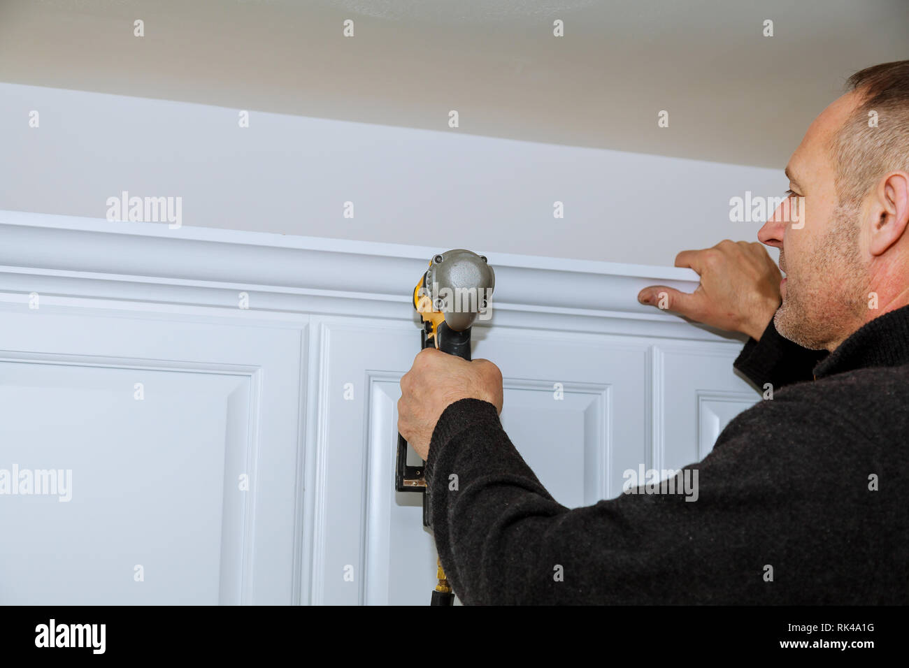 Handyman using brad nail gun on installation crown moulding wall