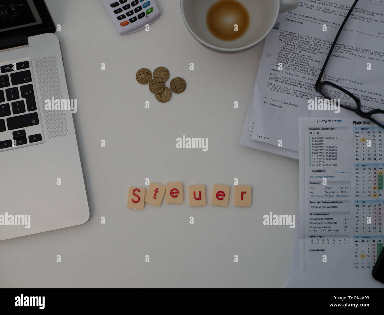 Top view of white desk with documents, glasses, notebook and letters saying "Steuer"  (Tax) Stock Photo